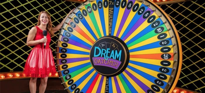 A woman in a red dress stands beside a large, colorful Dream Catcher wheel with various numbers and multipliers.