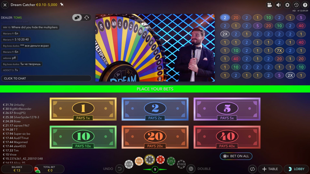 Ein Screenshot der Benutzeroberfläche des Online-Casinospiels "Dream Catcher". Das Hauptmerkmal ist ein großes, buntes Rad mit nummerierten Segmenten. Ein elegant gekleideter Moderator steht neben dem Rad. Darunter befinden sich Wetteinsatzoptionen für die Zahlen 1, 2, 5, 10, 20 und 40, jeweils mit unterschiedlichen Auszahlungsquoten. Die Benutzeroberfläche enthält ein Chatfenster, Spielerguthaben und Wetteinsatzsteuerungen.