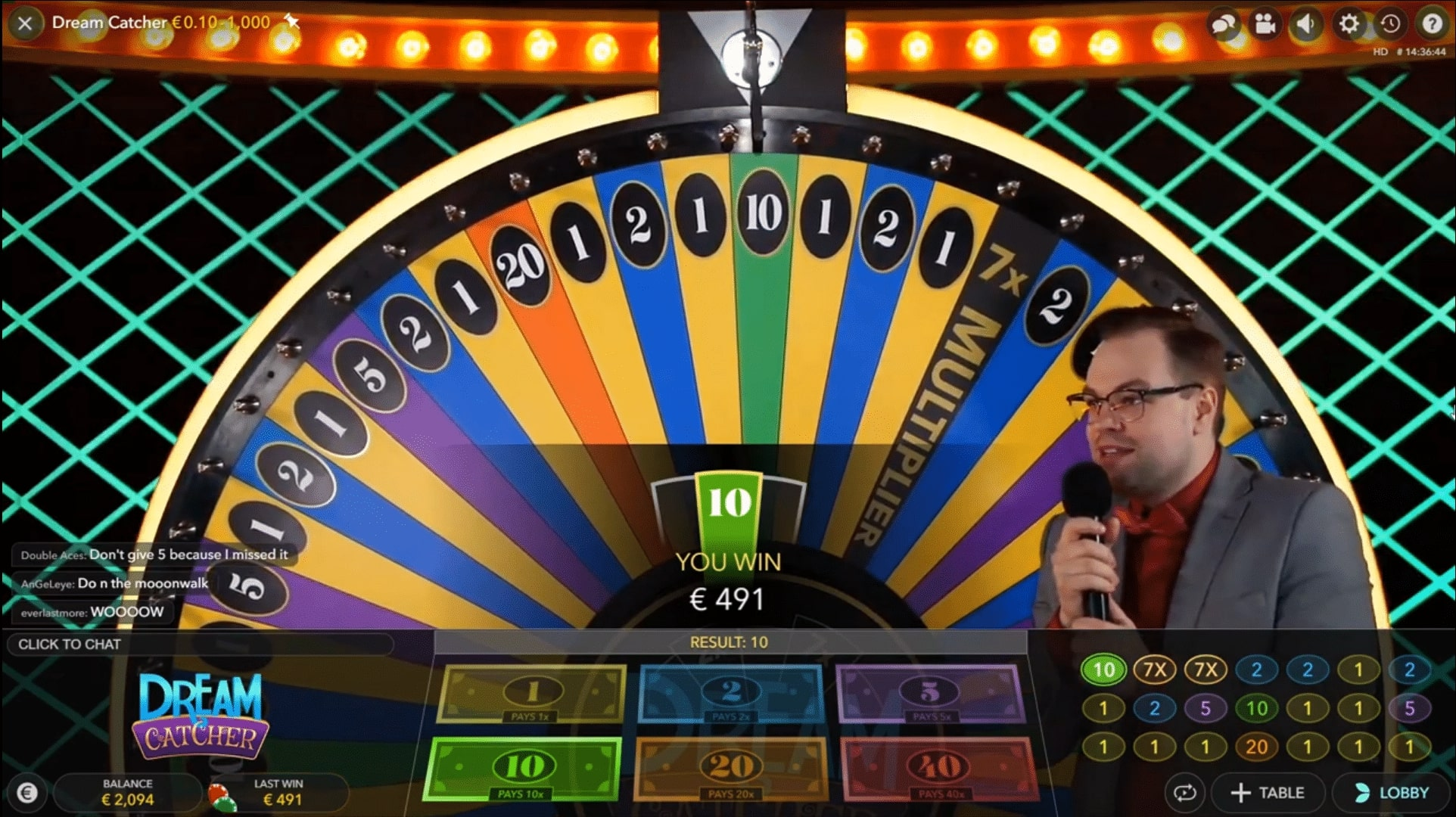 Uno screenshot del gioco "Dream Catcher" in corso. La ruota si è fermata sul numero 10, indicato da un segmento verde al centro. Un presentatore in giacca e cravatta rossa è visibile mentre parla al microfono. Lo schermo mostra "HAI VINTO €491" e indica il risultato e i moltiplicatori. Lo sfondo presenta una griglia di luci color acquamarina.